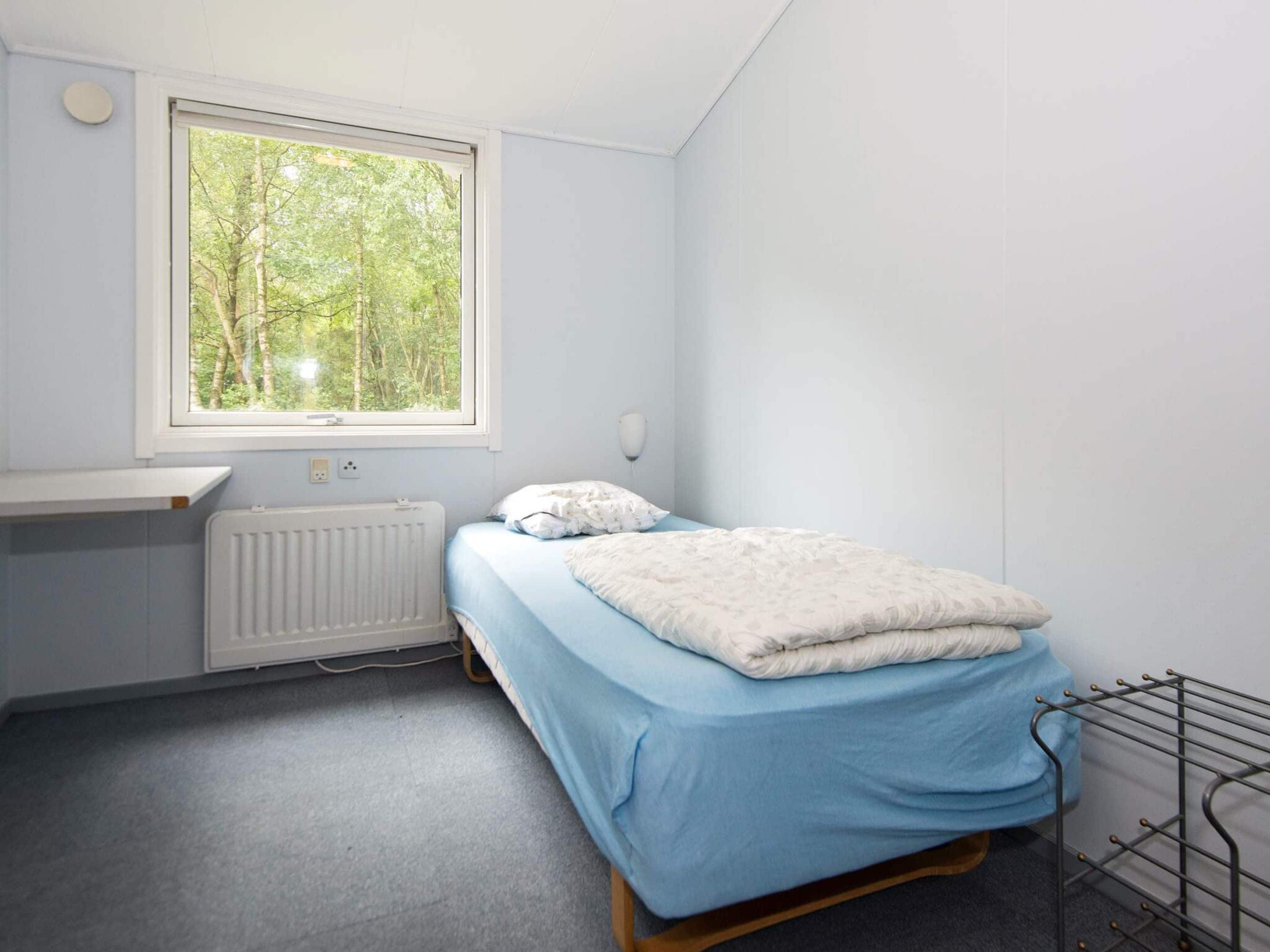 A small, single-bed room with a window overlooking a forest.
