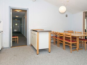 Un coin repas avec une table et des chaises en bois, une petite cuisine équipée d’un réfrigérateur et d’un évier, et un couloir menant à une autre pièce.
