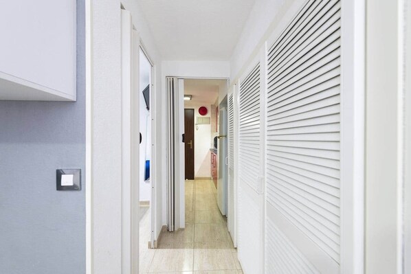 A narrow hallway with a door at the end leading to a room.