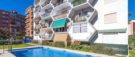 A modern apartment building with a hexagonal facade, a swimming pool, and balconies with railings.