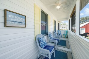 A porch with wicker chairs, a welcome sign, and a view of a red building.