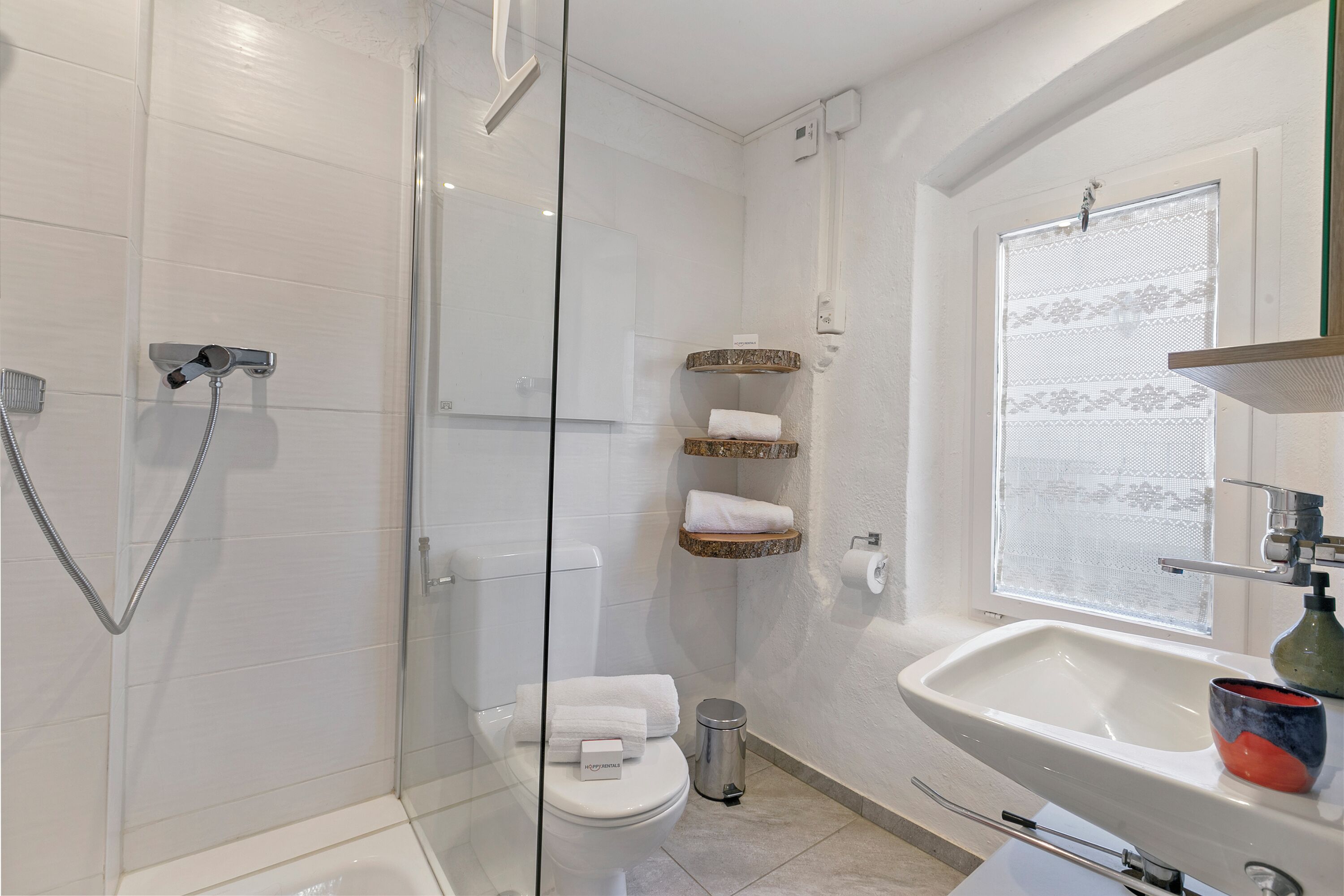 Une salle de bain moderne avec une douche à parois de verre, des toilettes et un lavabo placé sous une fenêtre.