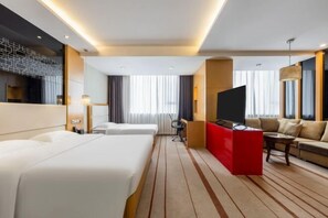 A hotel room with two beds, a red desk, a sofa, a TV, and a large window with curtains.