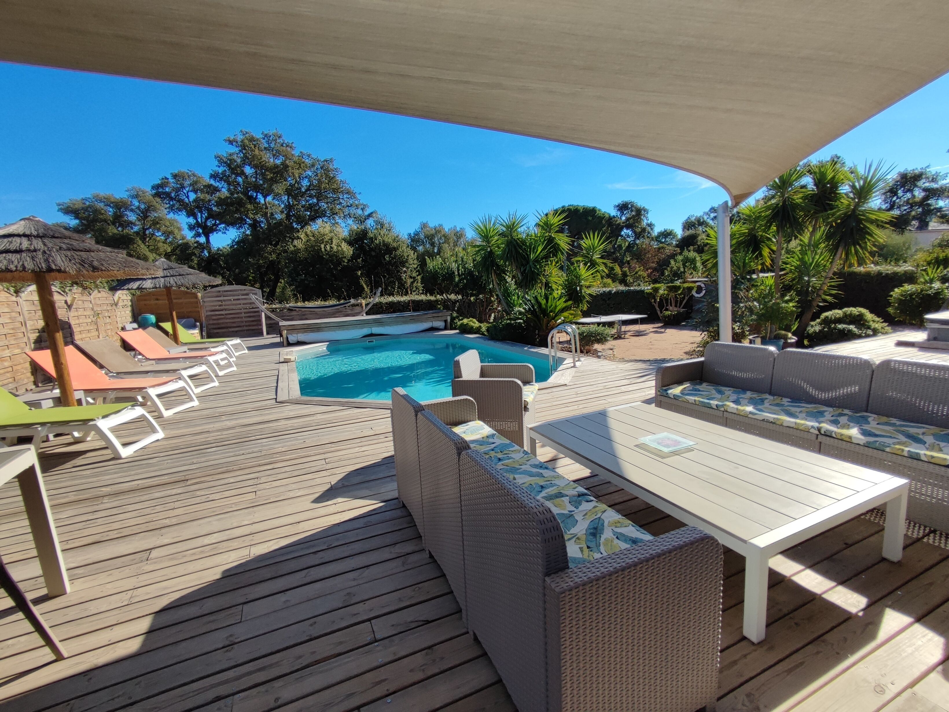 A wooden deck with a pool, lounge chairs, and a covered seating area.