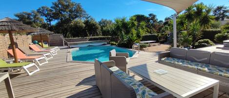 A wooden deck with a pool, lounge chairs, and a covered seating area.