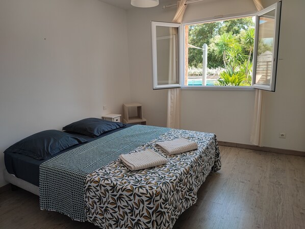 Una camera da letto con un letto, un comodino, una finestra con tenda aperta e vista su spazi verdi.