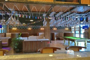 Zona de bar con mesa de billar, asientos e iluminación colgante.
