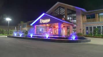 A hotel entrance with a covered area, illuminated by blue lights and a water fountain display.