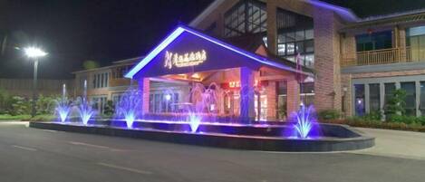 A hotel entrance with a covered area, illuminated by blue lights and a water fountain display.