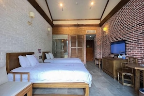 Una habitación de hotel con dos camas, cabecero de madera, televisor y pared de ladrillo.