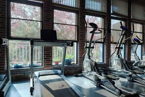 Un gimnasio con equipo de ejercicio, ventanas amplias y vistas a árboles.