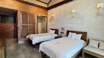 A hotel room with two beds, a wooden bench, a brick wall, and a glass door leading to a balcony.