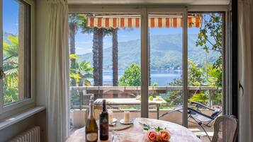 A room with a view of a lake, a table with bottles and flowers, and a chair.