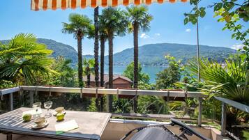 A balcony with a table, chairs, and a view of a lake and mountains.