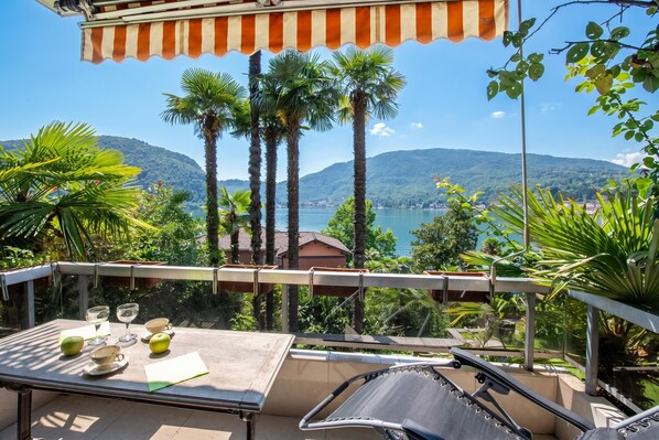 A balcony with a table, chairs, and a view of a lake and mountains. - Queen Lake View Apartment With Terrace (Tresa)