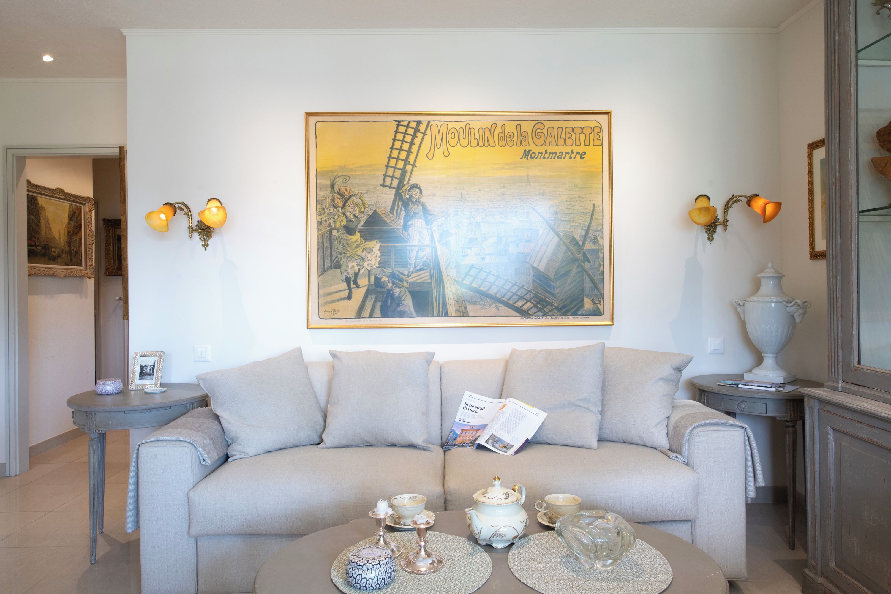 A living room with a beige sofa, a coffee table with tea sets, and a framed poster on the wall.