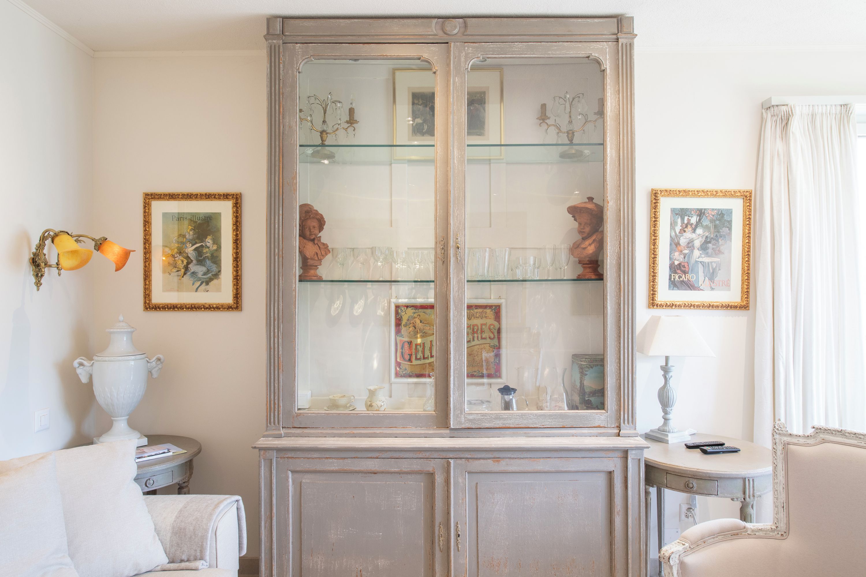 A room with a vintage cabinet displaying glassware and framed pictures.