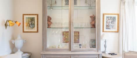Une pièce dans laquelle se trouve un meuble ancien servant de vitrine pour des objets en verre et des tableaux encadrés.