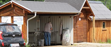 A small wooden building with a metal roof, a man standing at a sink, and a car parked in front.