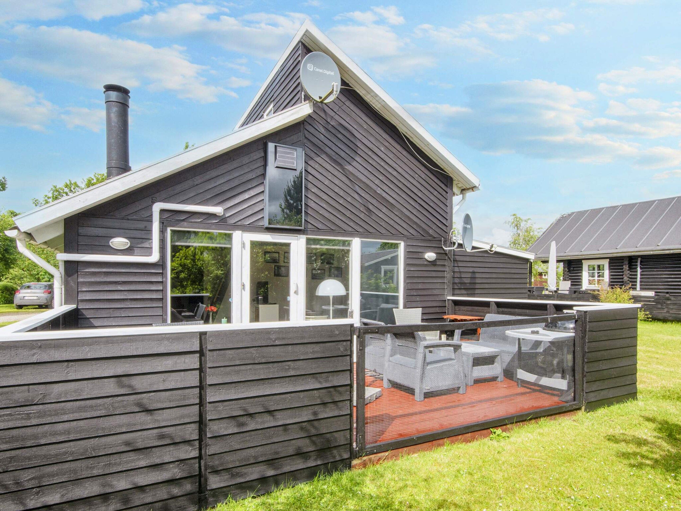 A modern house with a large deck, a chimney, and satellite dishes.