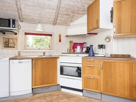 Una cocina compacta con armarios de madera, un lavavajillas blanco, una estufa y un microondas.