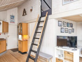 Una habitación con una escalera de madera apoyada en una pared, un televisor sobre un pedestal blanco y una puerta con un letrero que dice 'No molestar'.