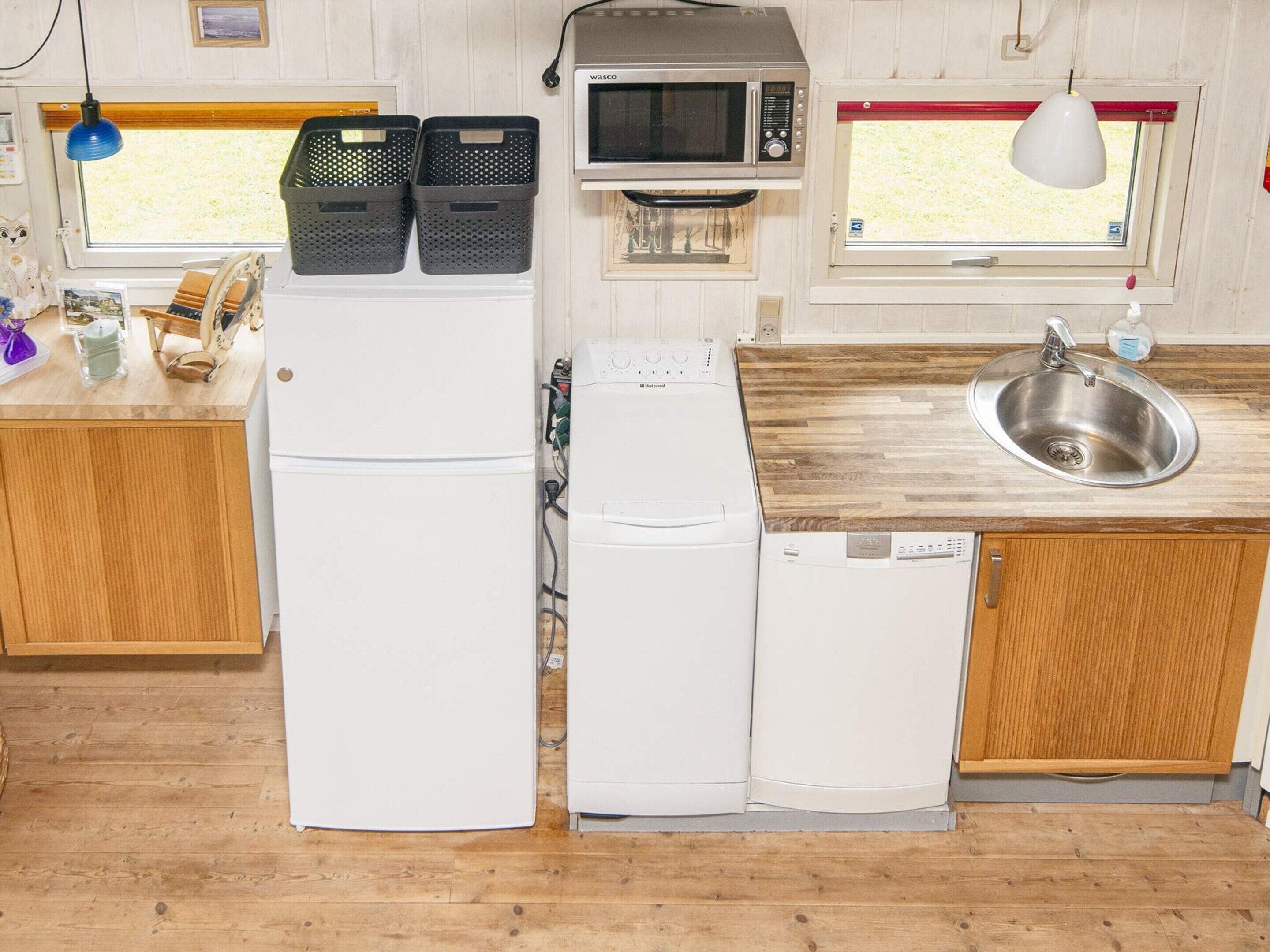 Cozinha compacta equipada com frigorífico, micro-ondas, máquina de lavar loiça e lava-loiça.