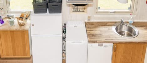 Cozinha compacta equipada com frigorífico, micro-ondas, máquina de lavar loiça e lava-loiça.