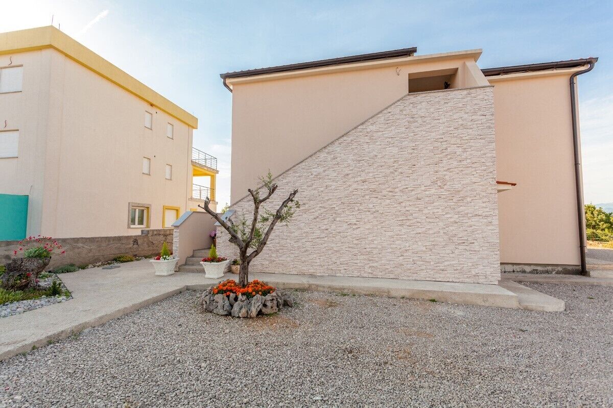 A building with a beige exterior, a stone facade, and a small tree in the foreground.