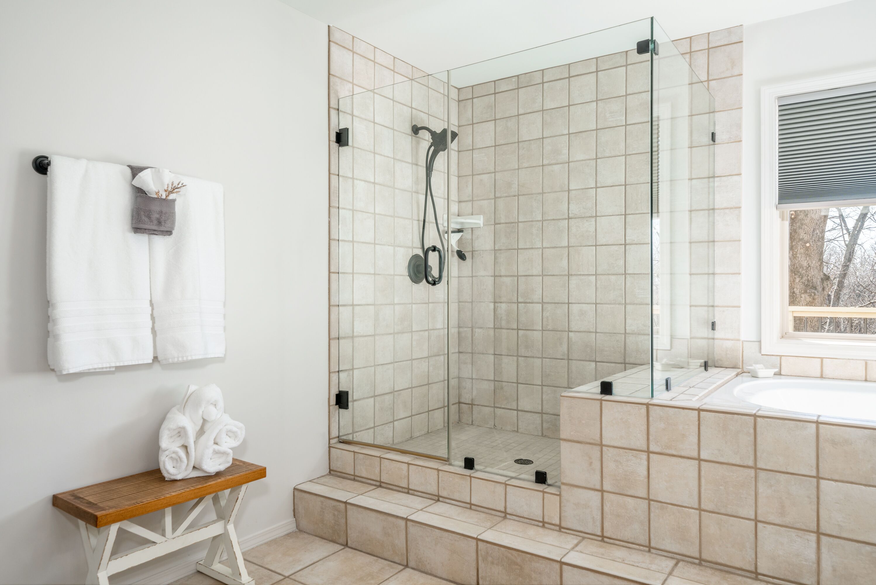 A modern bathroom with a glass-enclosed shower, a wooden bench, and a large mirror.