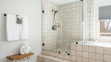 A modern bathroom with a glass-enclosed shower, a wooden bench, and a large mirror.
