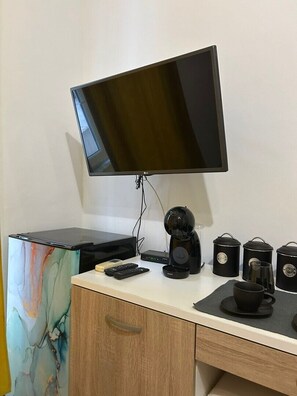 Une chambre moderne dotée d’un téléviseur à écran plat fixé au mur, d’un petit bureau avec une machine à café, une télécommande et des boîtes de rangement.