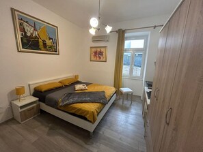 Une chambre à coucher comprenant un lit, des tables de chevet, une armoire, une fenêtre avec des rideaux et des œuvres d’art murales.