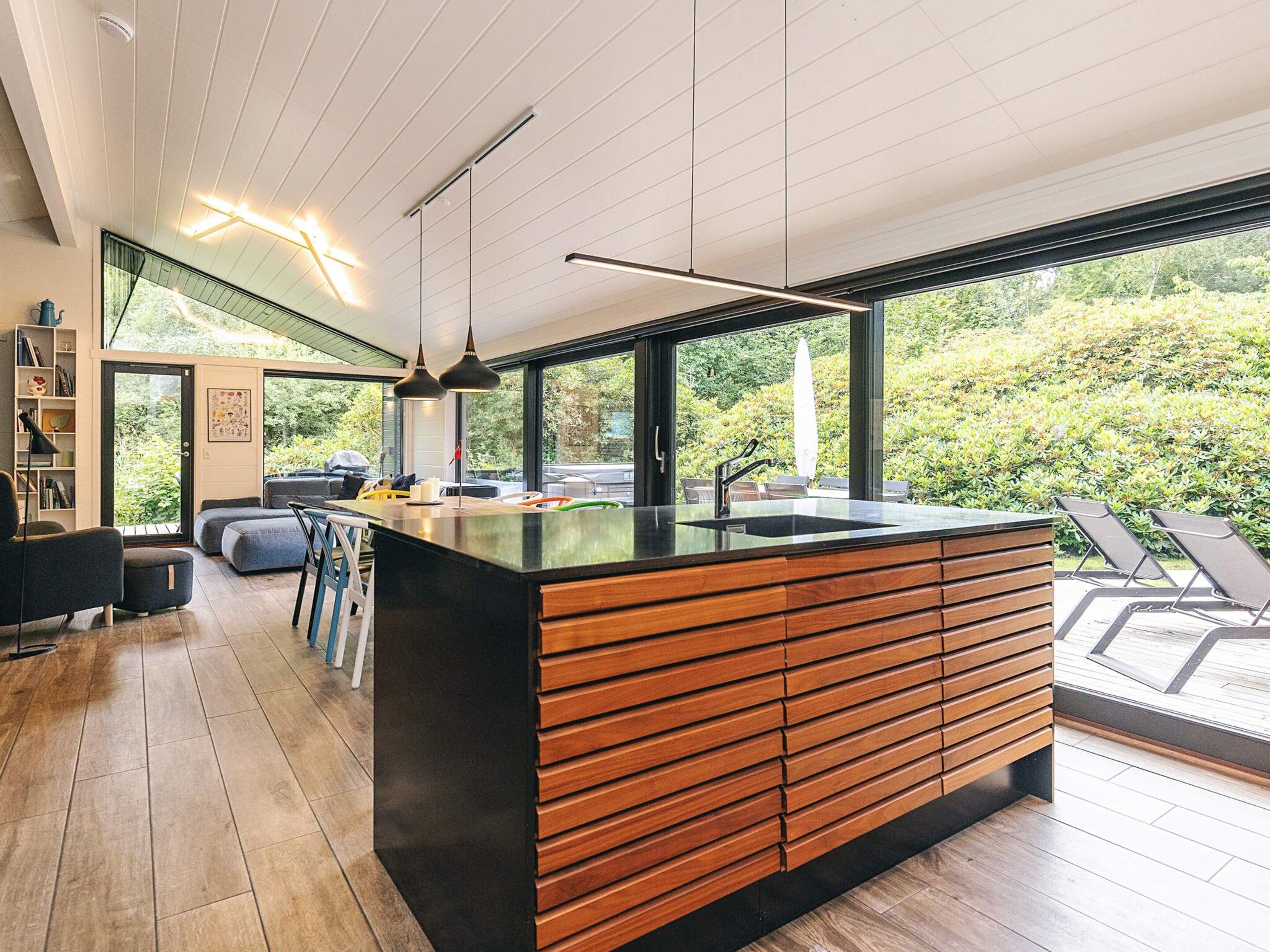A modern kitchen with a large island, wooden cabinetry, and a view of the outdoors.