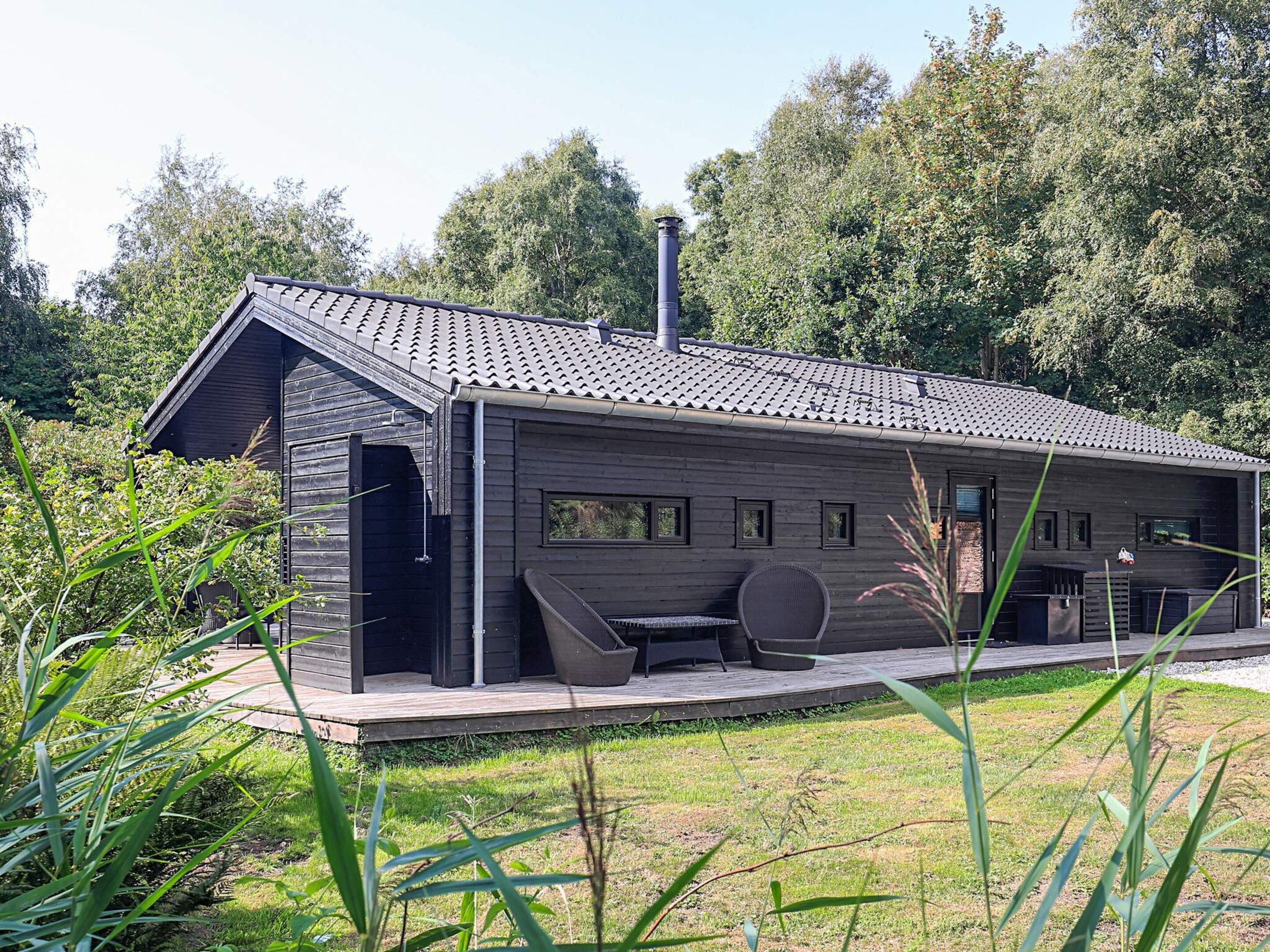 A modern wooden cabin with a sloped roof, a chimney, and a deck with outdoor seating.