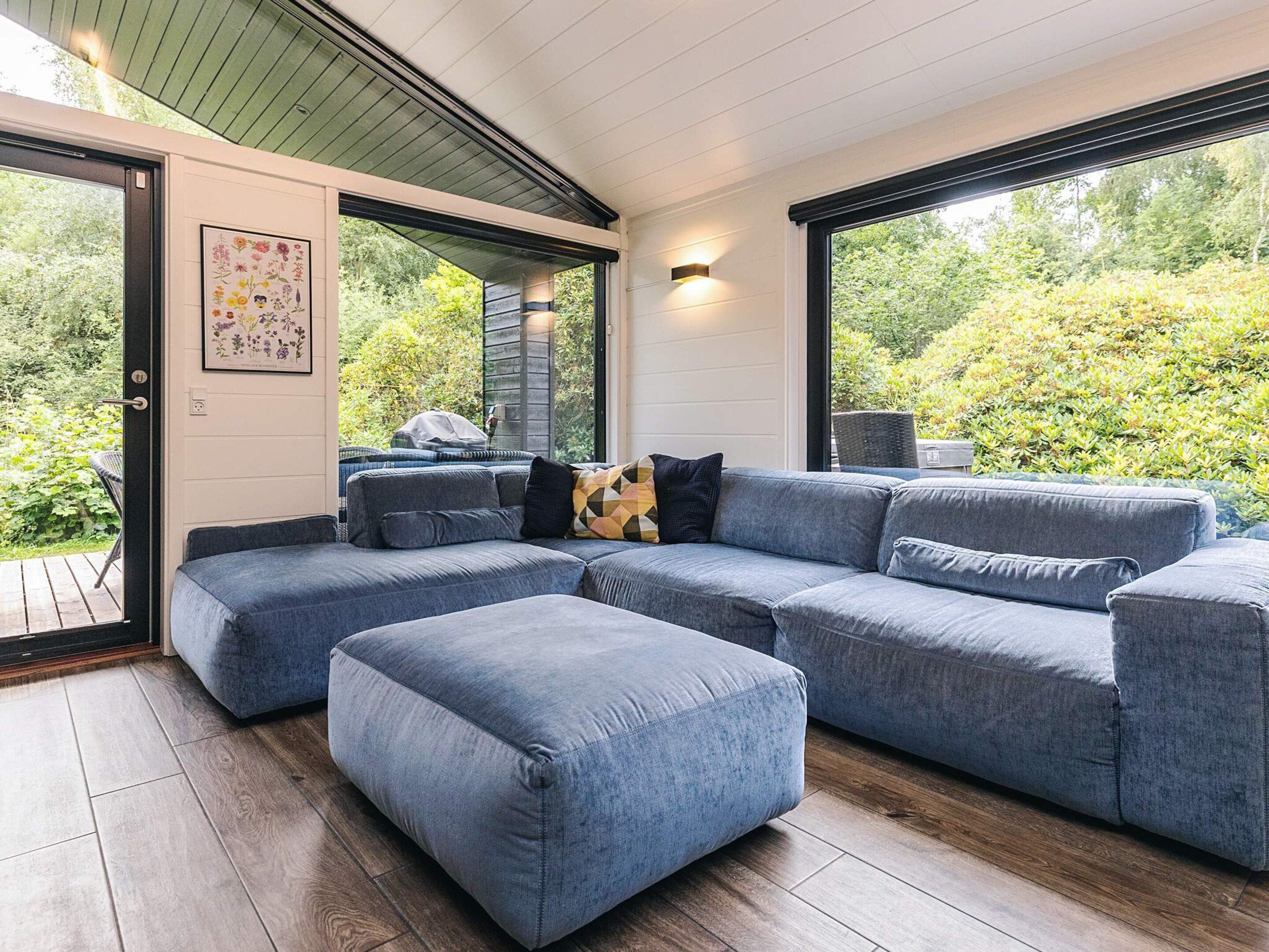 A modern living room with a sectional sofa, a small ottoman, and a large window offering a view of greenery.