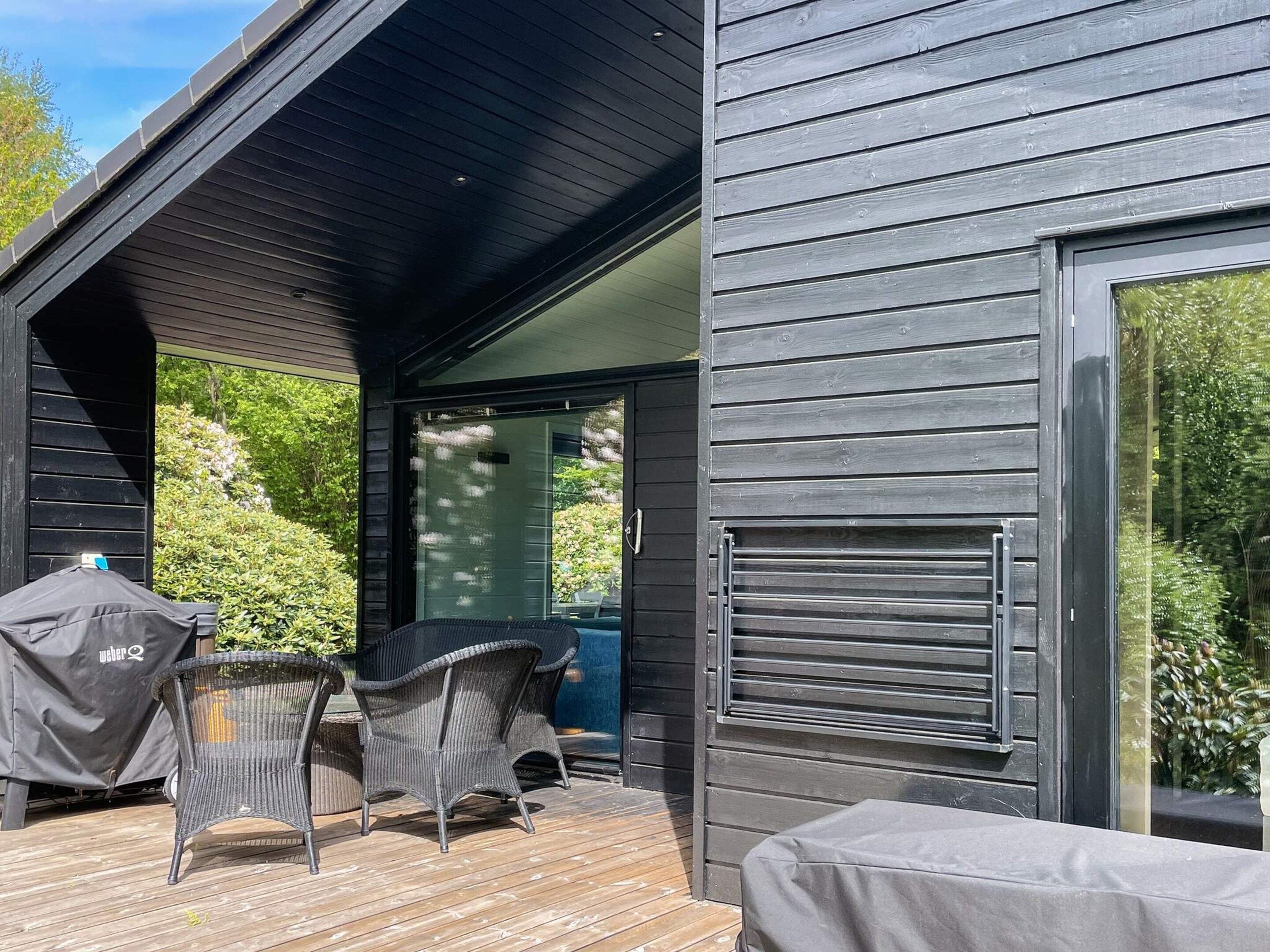 A covered outdoor area with a grill, wicker chairs, and a table.