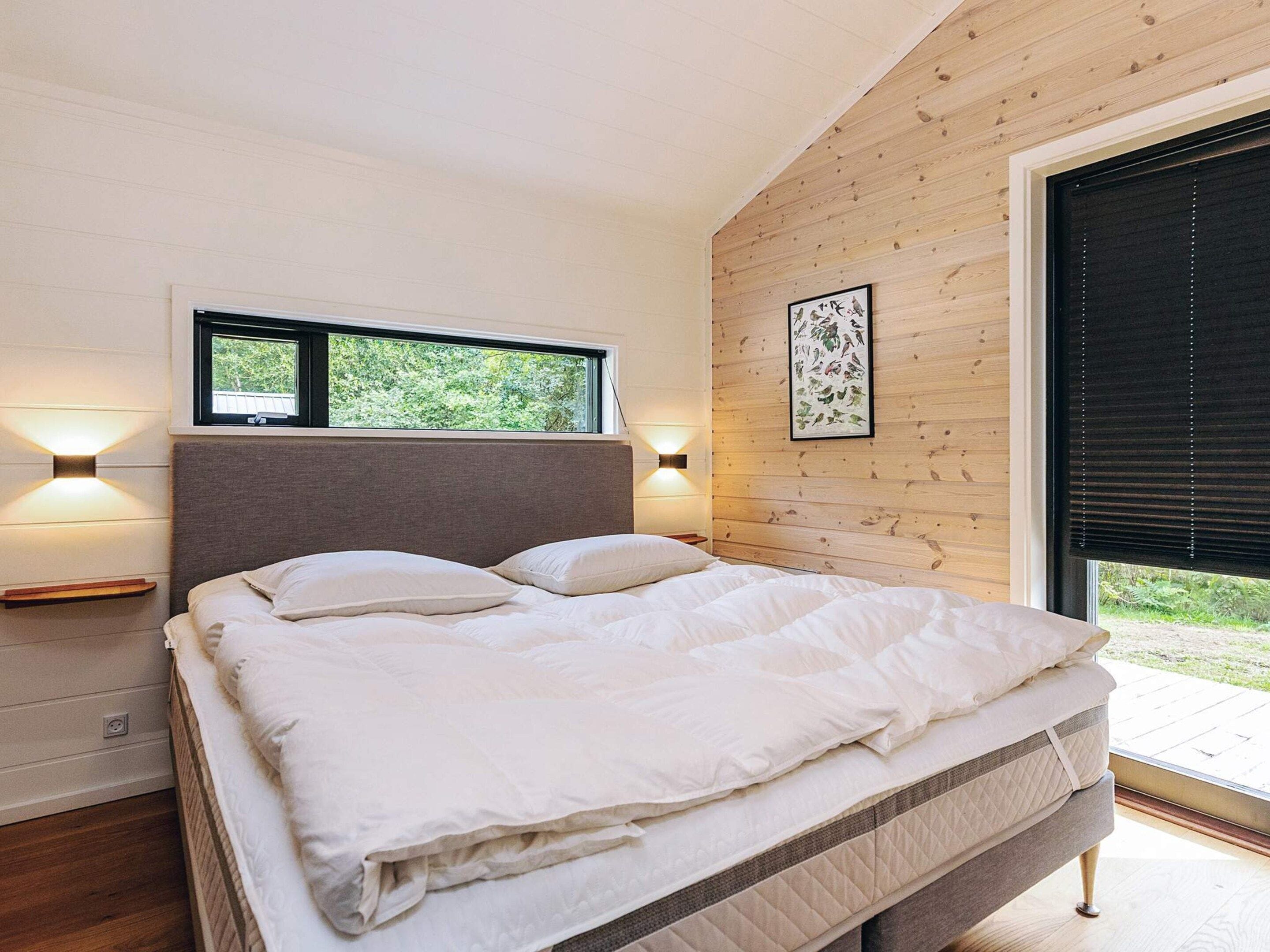 A bedroom with a bed, two wall-mounted lights, a window, and a picture on the wall.