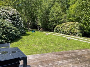 A wooden deck with a table and chairs, a well-maintained lawn, and a path leading through a wooded area.