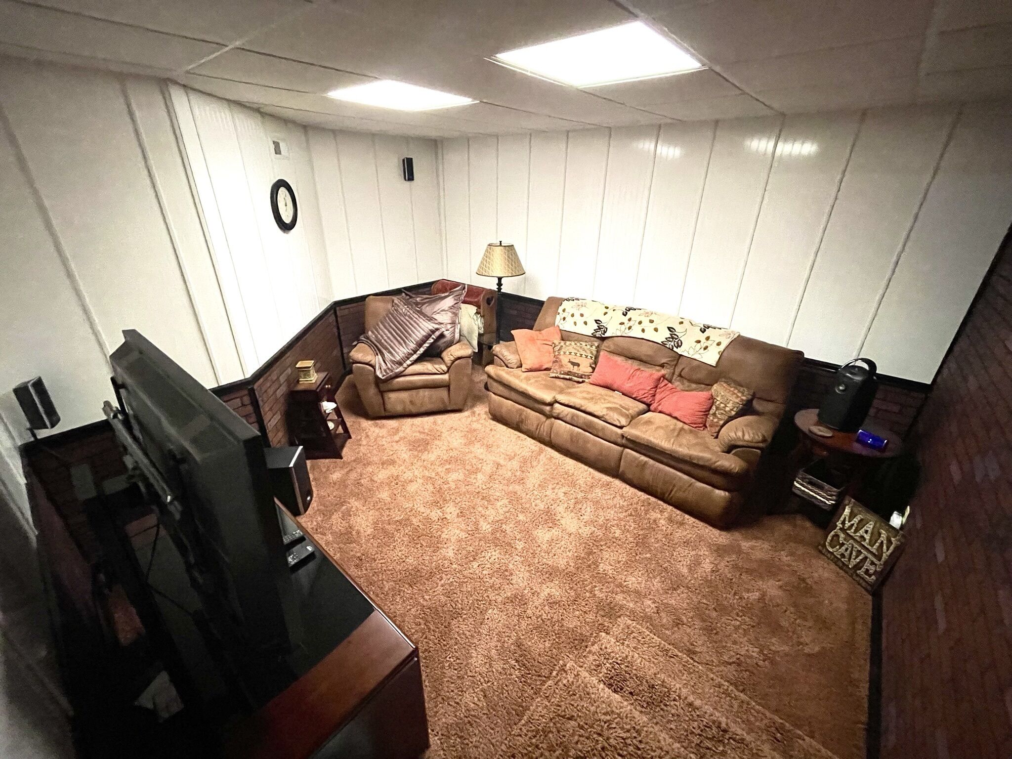 Un salón con un sofá de cuero marrón, un sillón marrón, un televisor y una lámpara.