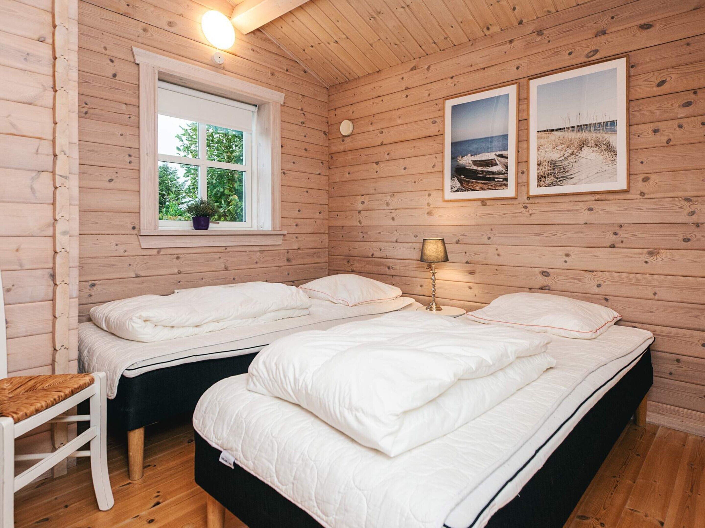 Une chambre de style cabane avec deux lits, une fenêtre donnant sur un paysage verdoyant et deux tableaux encadrés accrochés au mur.