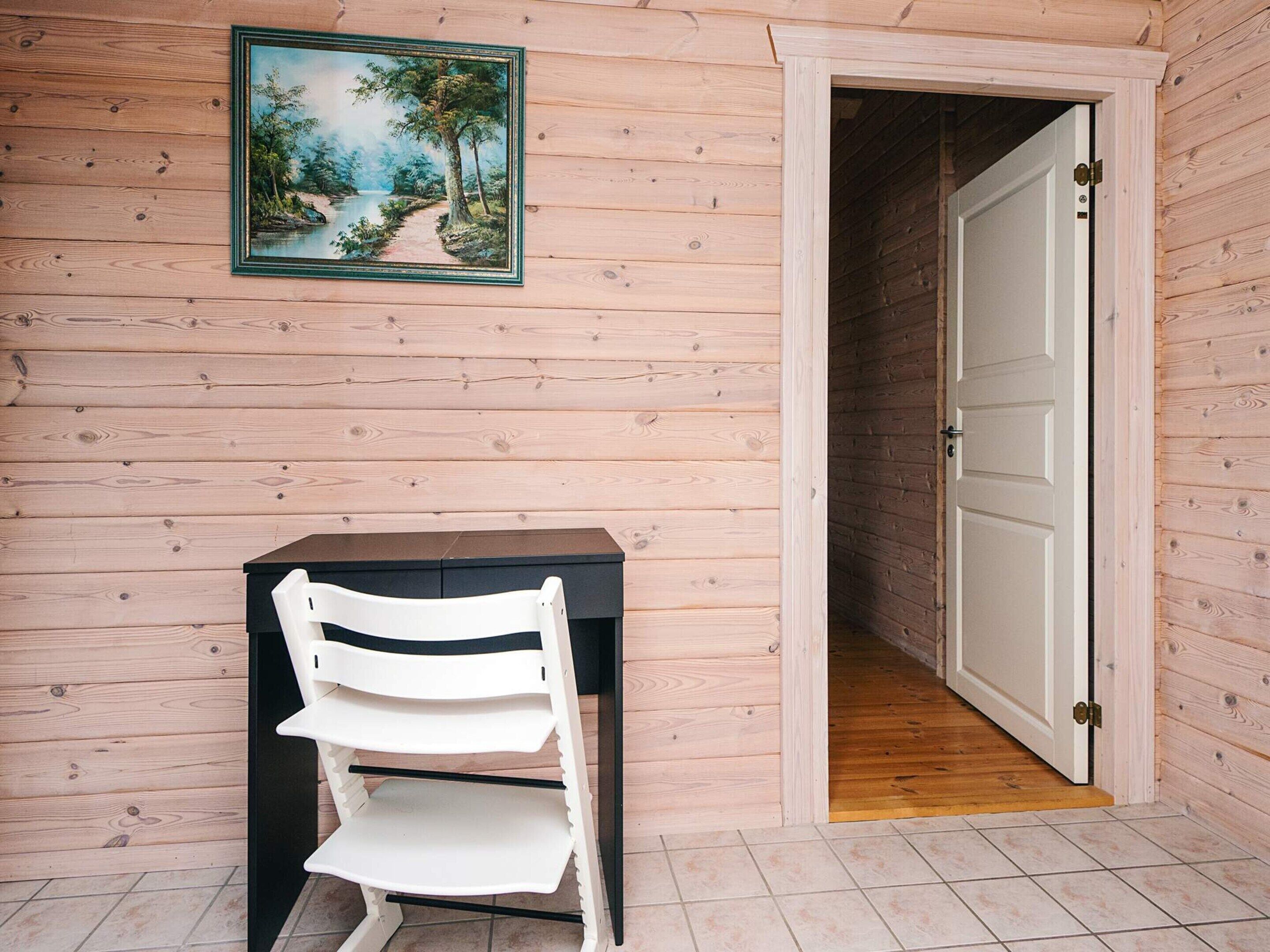Une pièce en bois avec une chaise blanche, une petite table et une porte qui donne sur une autre pièce.