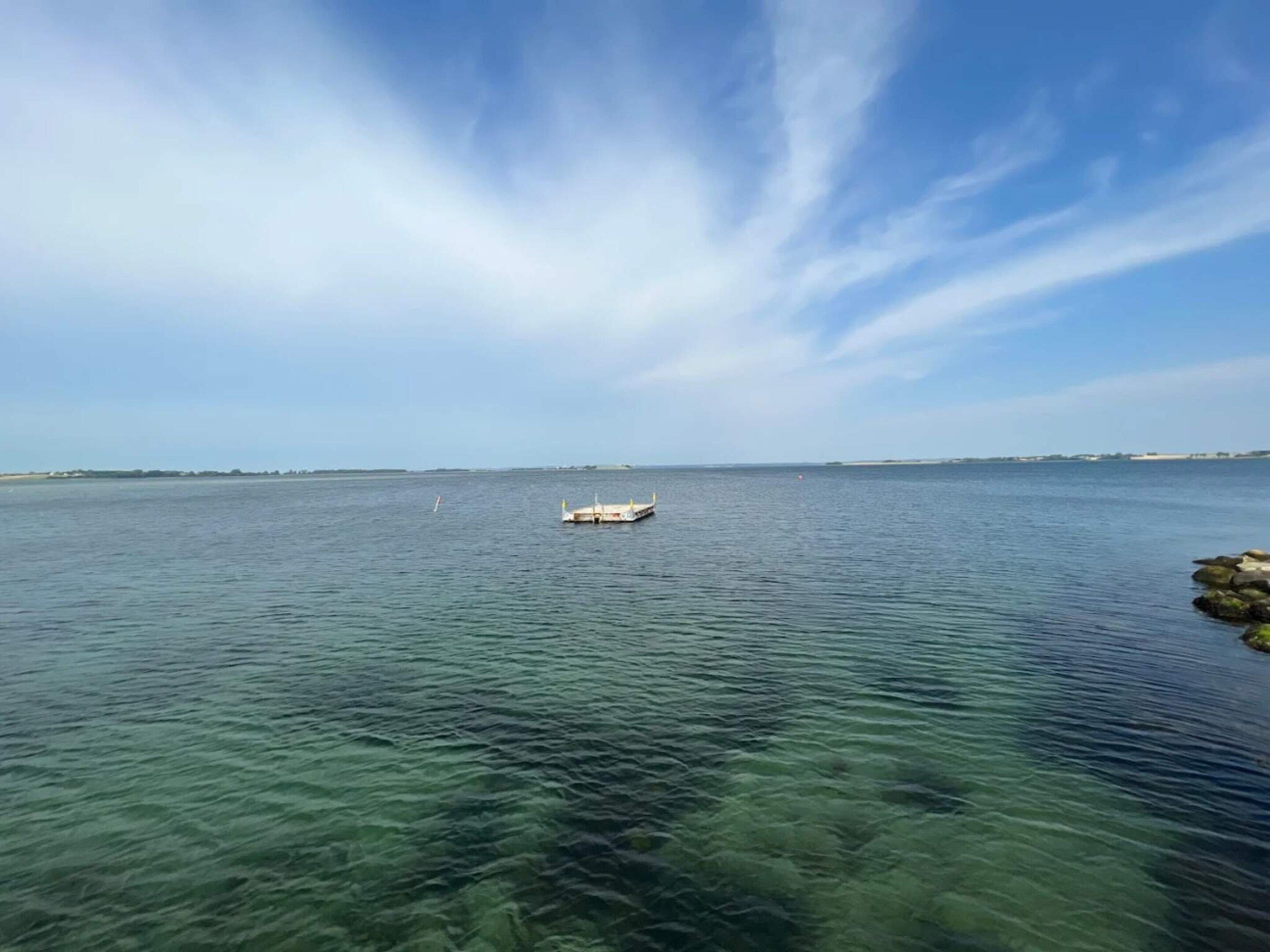 Una masa de agua tranquila con un barco pequeño a lo lejos y un cielo despejado.