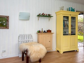 A room with a wooden floor, a white picket fence, a small stool with a fur throw, a yellow cabinet with glass doors, and a green shelf with decorative items. - 6 Person Holiday Home in Knebel (Knebel)