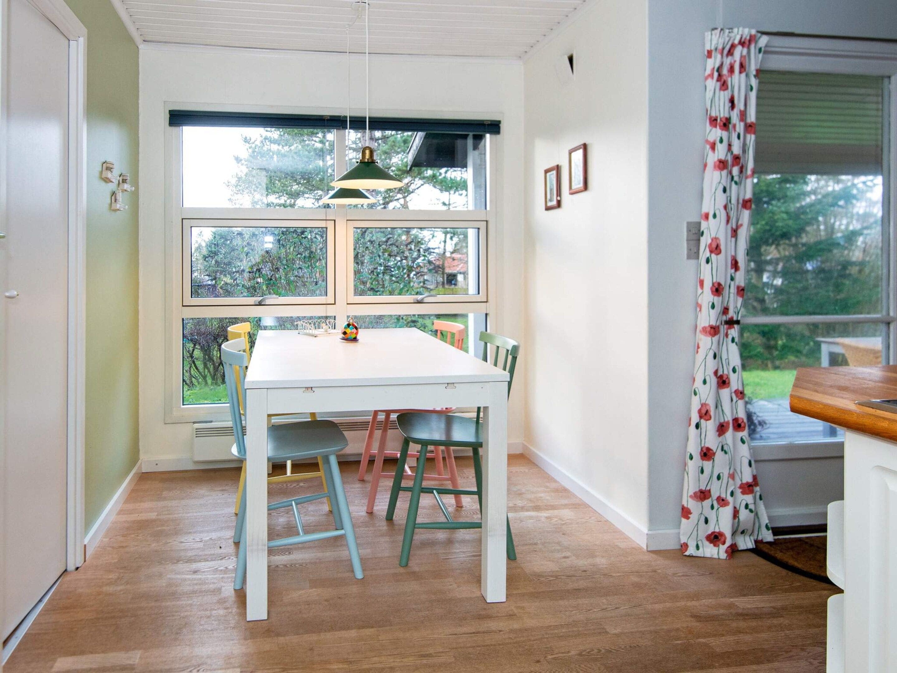 A dining area with a white table and chairs, a hanging pendant light, and a window with a view of greenery.