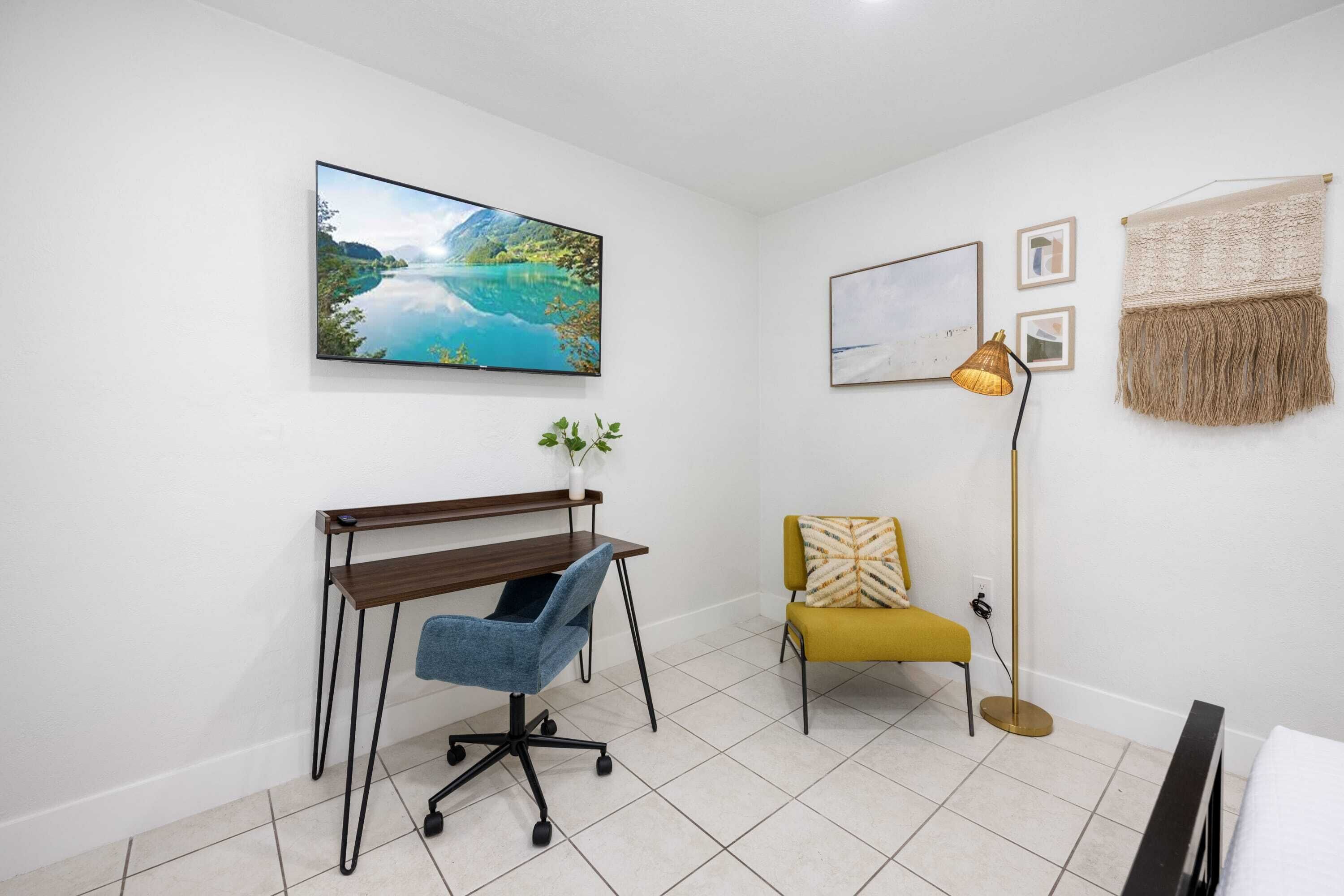 A room with a desk, chair, and a television mounted on the wall.