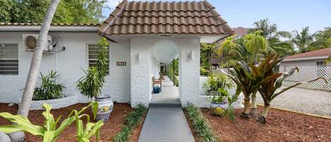 A residential property with a covered porch, a pathway leading to the entrance, and a variety of plants and trees.