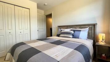 A bedroom with a large bed, a wooden headboard, a nightstand with a lamp, and a closet with white doors.