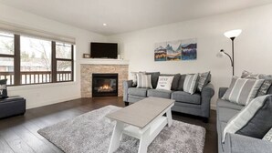 A living room with a fireplace, grey sofas, a coffee table, and artwork on the wall. - Central A/C Townhouse Mt.Views | Fireplace | Garage | Deck (Invermere)