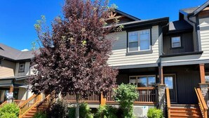 A two-story house with a front porch, a staircase, and a large tree in the front yard. - Central A/C Townhouse Mt.Views | Fireplace | Garage | Deck (Invermere)